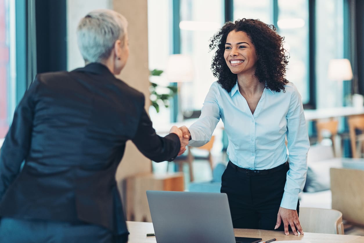 Two businesswomen shaking hands in a modern office setting, symbolizing a successful partnership or agreement.